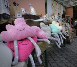 Zdjęcie, różowe poduszki w kształcie chmurki z nogami leżą na stoisku z rękodzielem