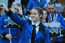 Zdjęcie, wokalistka kieruje mikrofon w stronę publiczności, w tle orkiestra dęta