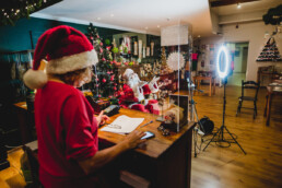 Zdjęcie, na pierwszym planie osoba w czapce Mikołaja stojąca tyłem do obiektywu, w tle Mikołaj w trakcie rozmowy przez smartfon