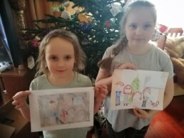 Zdjęcie, dwie dziewczynki trzymające w rękach swoje rysunki, na rysunkach - ich rodziny