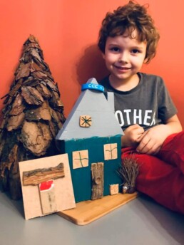 Zdjęcie, chłopiec prezentuje przygotowany przez siebie drewniany domek