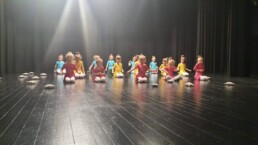 Zdjęcie_ Grupa taneczna małych dziewczynek siedzi na scenie. Przed sobą każda z nich ma małą poduszeczkę.