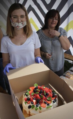 Zdjęcie, dwie kobiety pokazują ciasto umieszczone w kartonie
