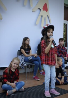 Zdjęcie, dziewczynka w trakcie śpiewania piosenki, w tle inni wokaliści