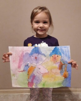 Zdjęcie, dziewczynka prezentuje swój rysunek, trzyma go w rękach