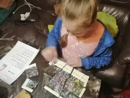Zdjęcie, dziewczynka siedząca przy biurku, układająca z puzzli mapę miasta; kadr z góry