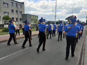 Miejska Orkiestra Dęta Lubliniec idzie ulicą w czarno niebieskim stroju grając na instrumentach 